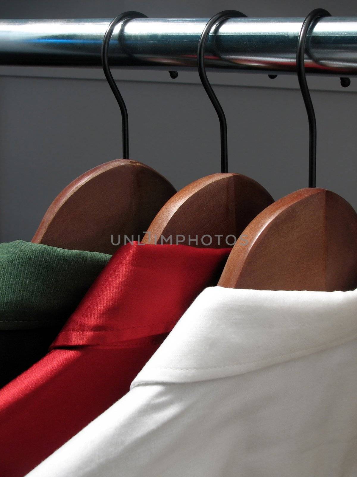 Green, red and white shirts on wooden hangers in a closet.