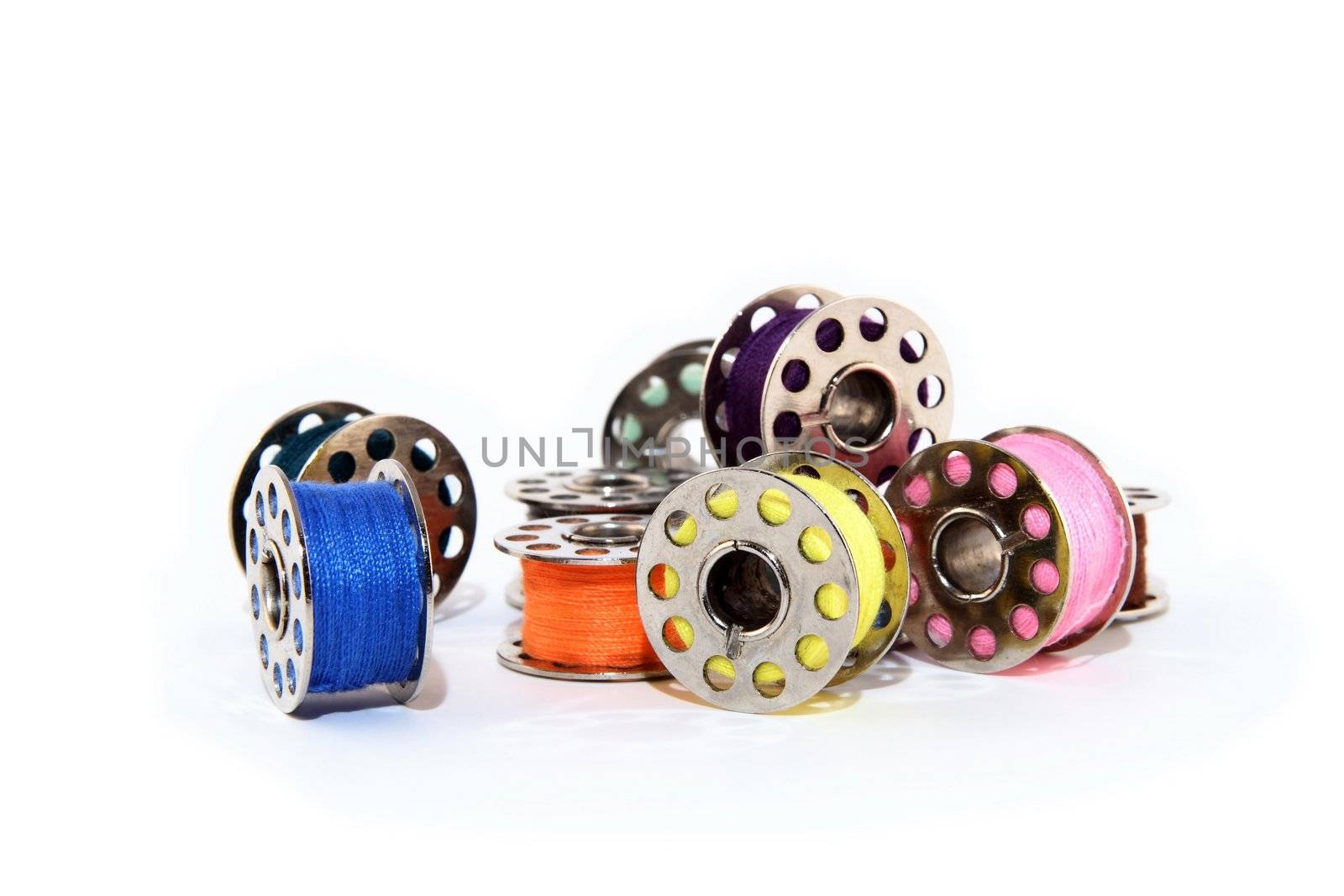 Pile of colorful thread spools for sewing machine, on white background.