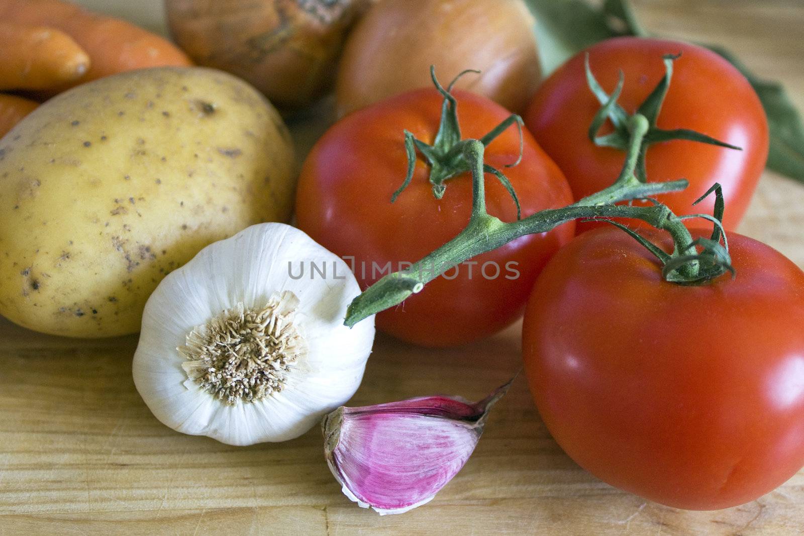 Some carrots, potatoes, onions, tomatoes, garlic and laurel on chopping board.