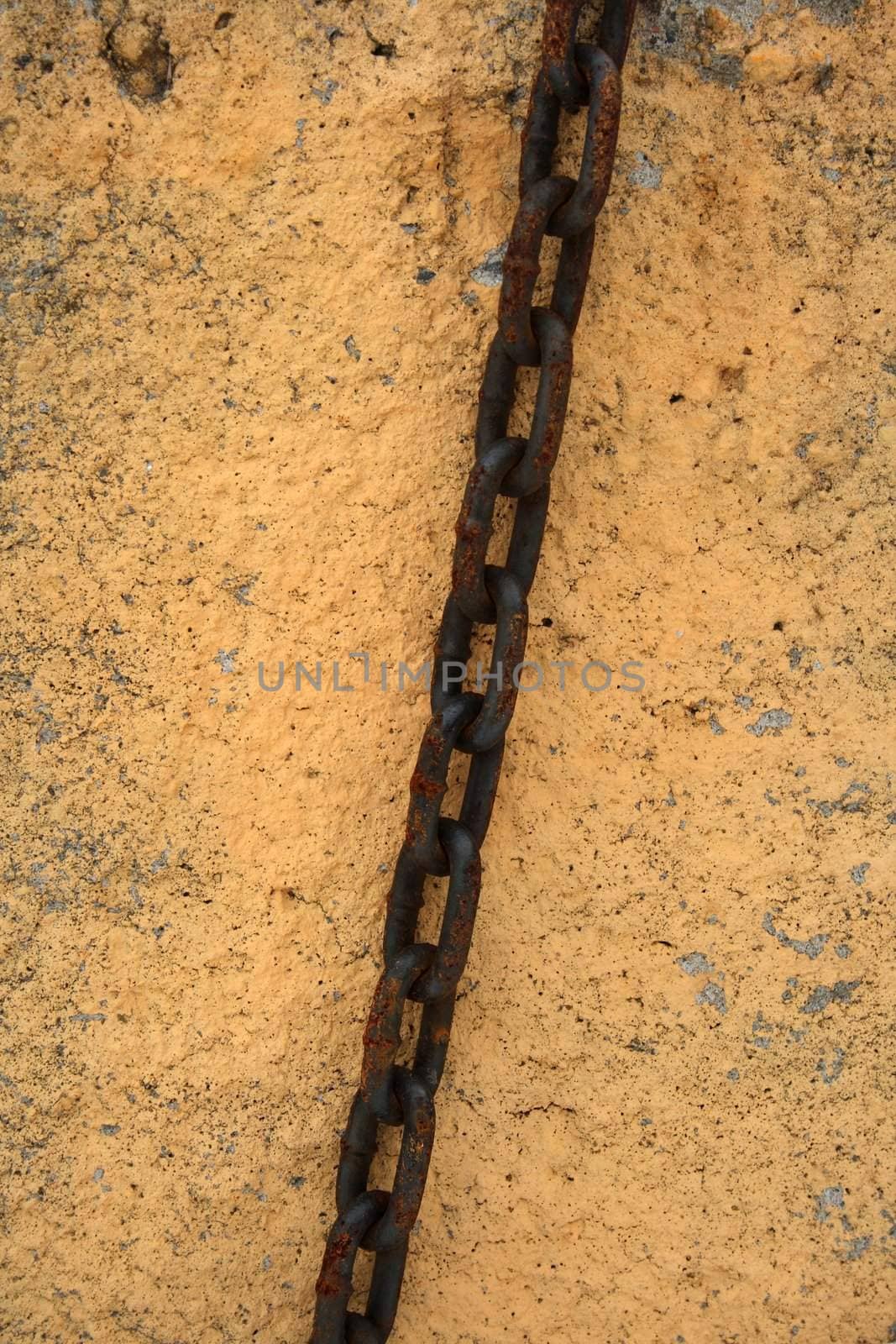 Rusty chain on a painted stone wall.