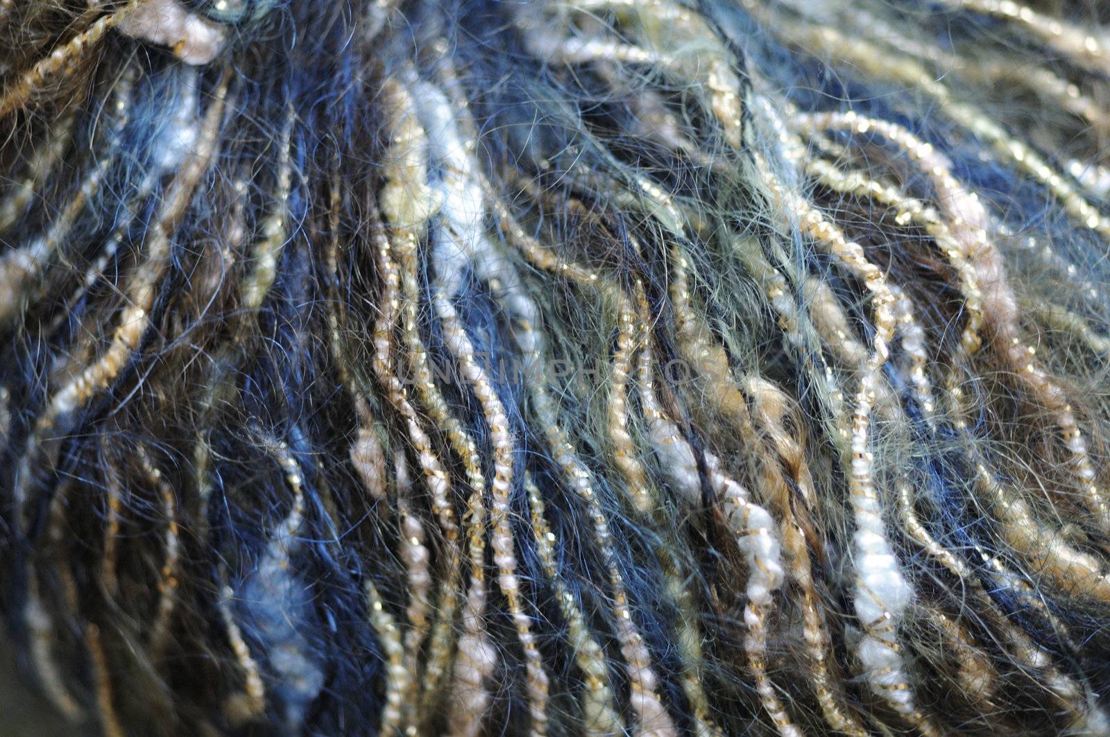 Close-up texture of a variegated ball of soft fuzzy yarn in tones of blue, gold, green, and white.  Curvy lines of yarn radiate out from the top center.