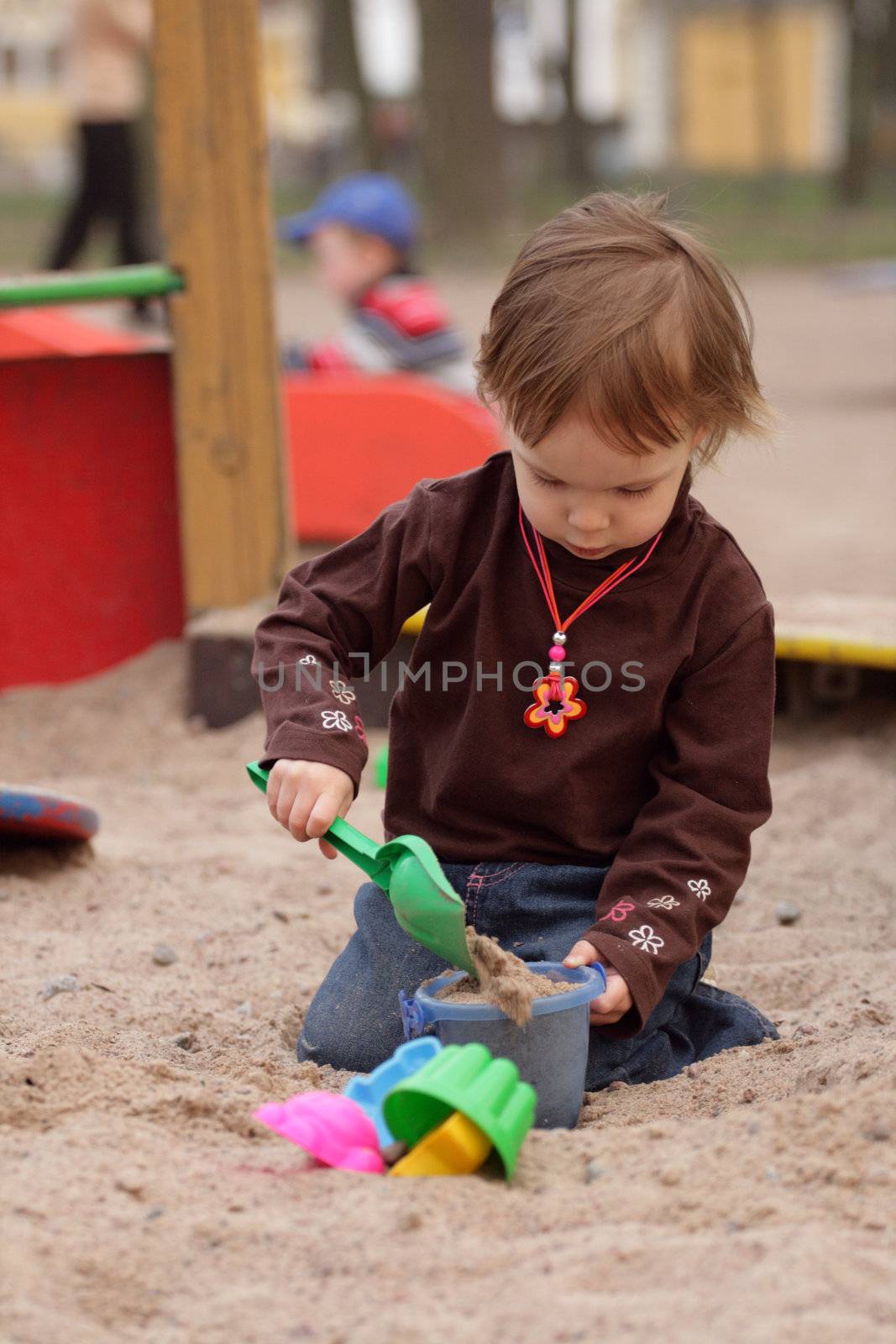 little beauty girl playing at sand-box. She with enthusiasm model of sand. 