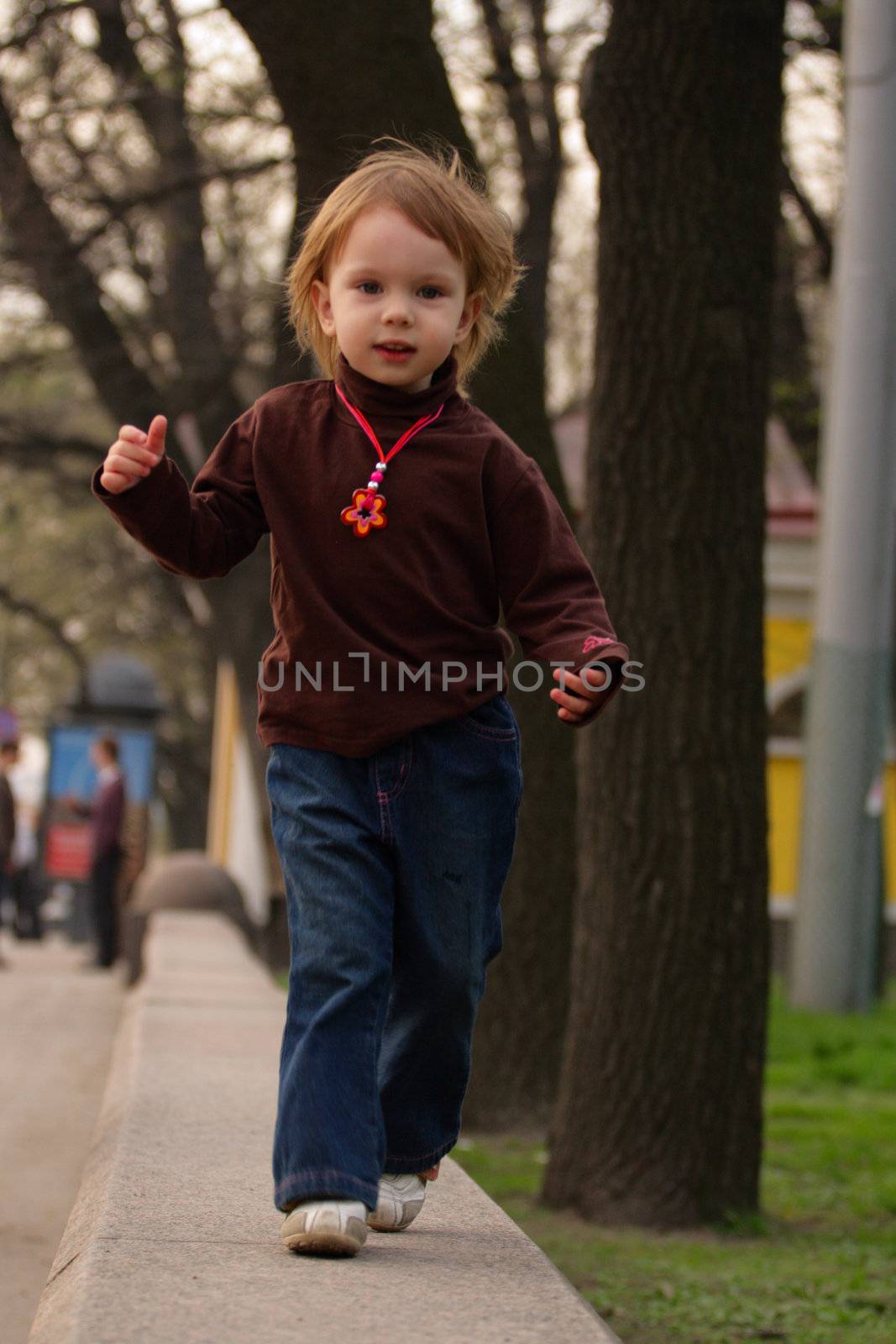 Little beauty girl running to photographer or audience on granit  narrow enclosure of park.