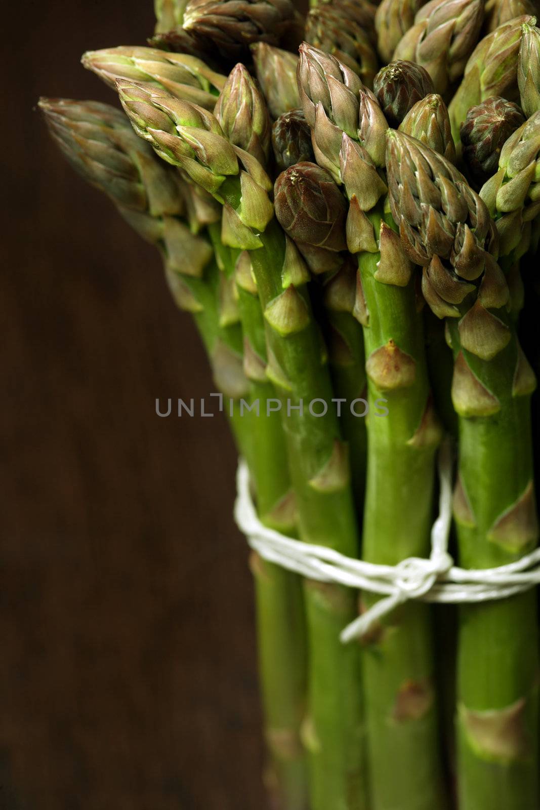 Bunch of asparagus on a wooden table.  Shallow depth of field, focusing on the tips.
