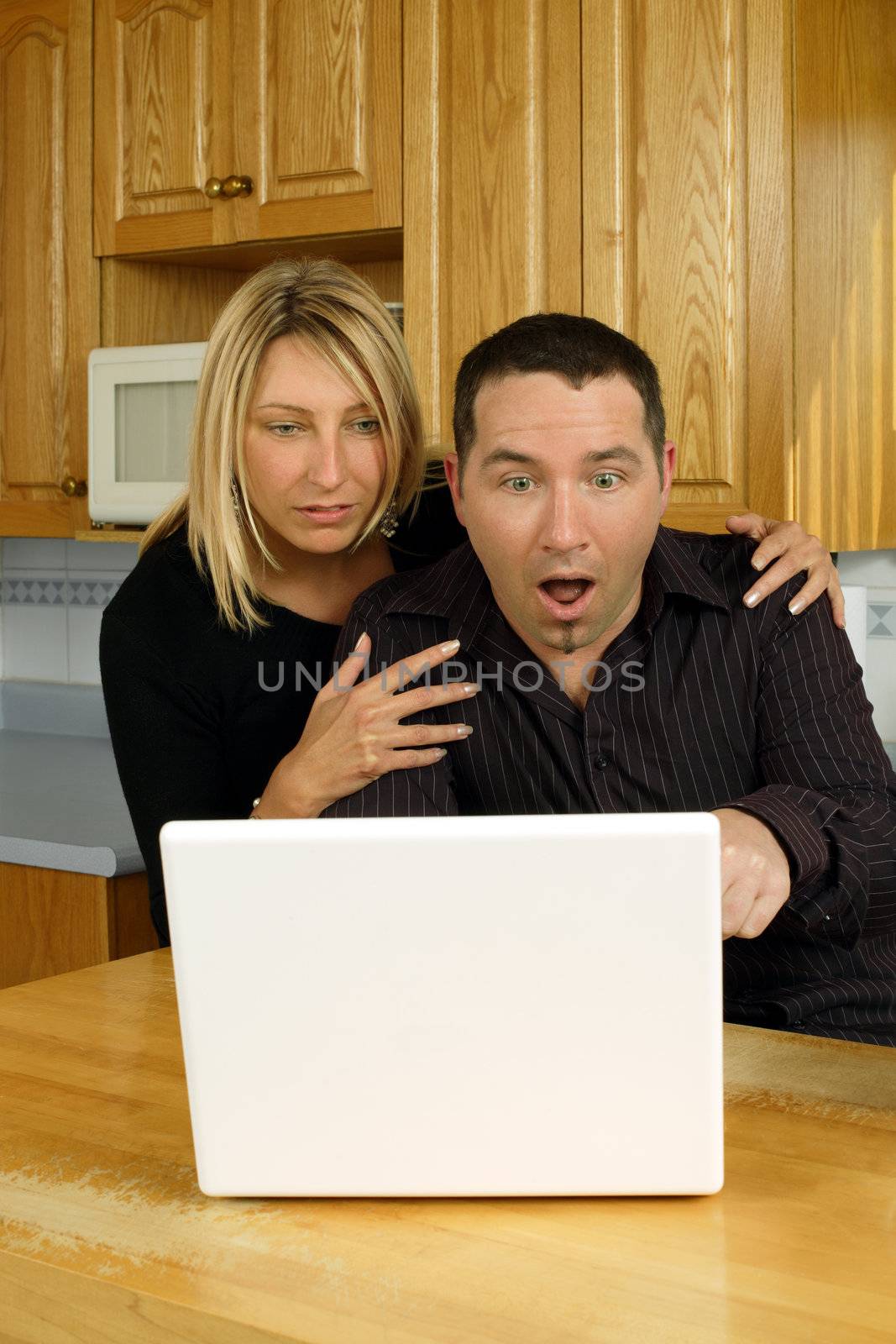 A loving couple, searching the internet on their laptop in their kitchen, and discovering something shocking.
