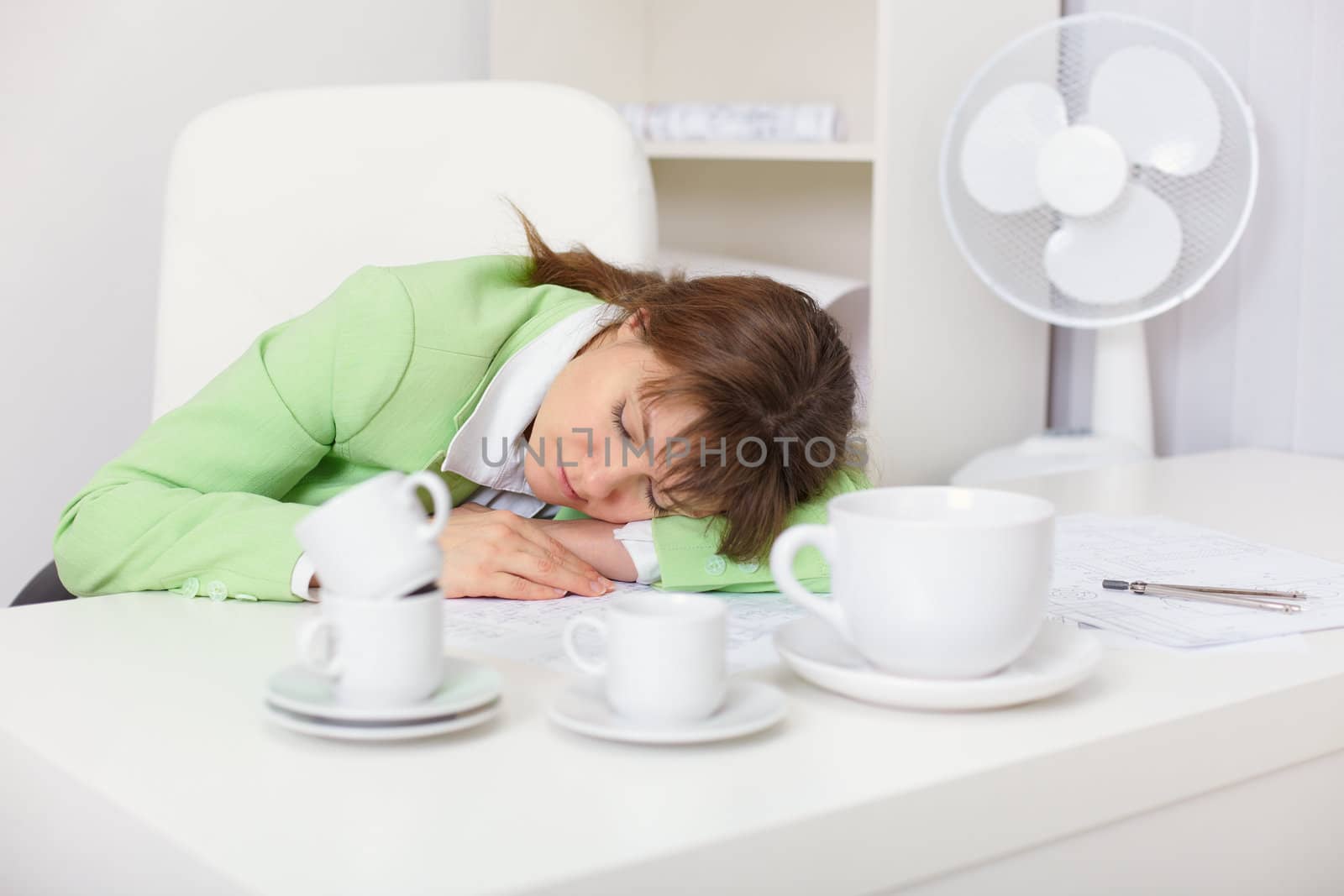 Tired woman sleeping on the desk in the office among the coffee cups