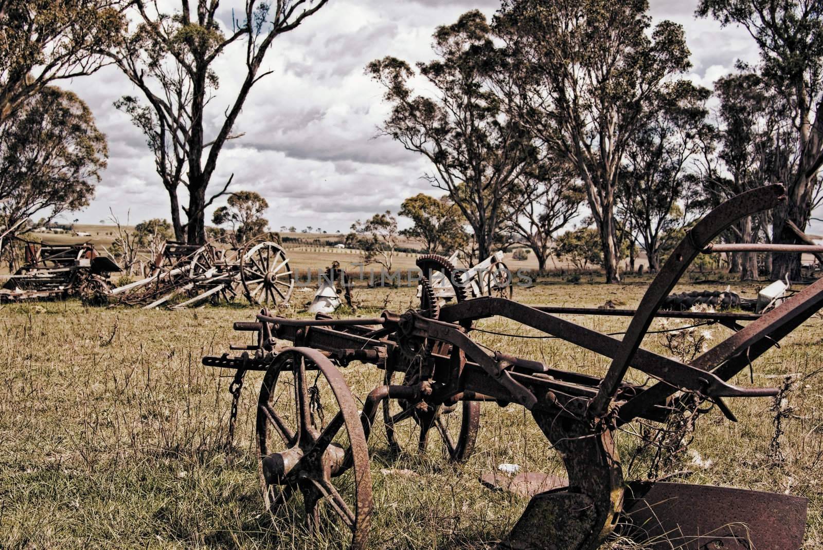 an old rusting horse drawn plow and machinery sits in the farm paddock 