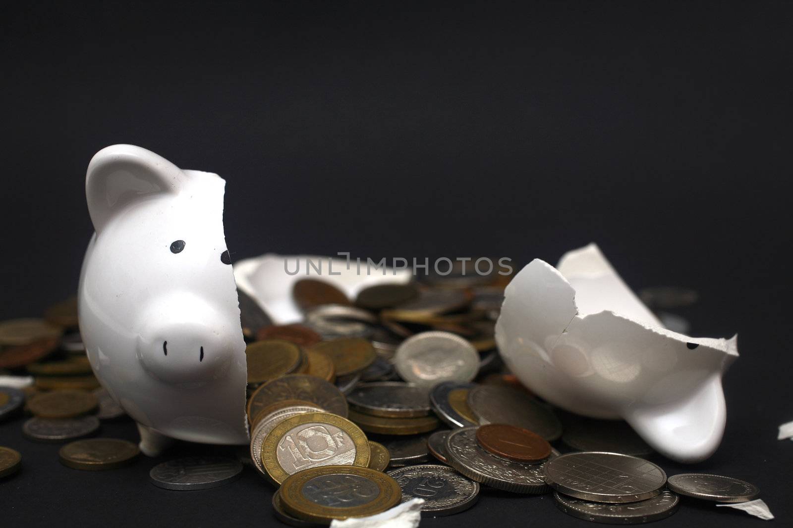 A broken piggy bank isolated on a dark background with loads of coins from around the world.