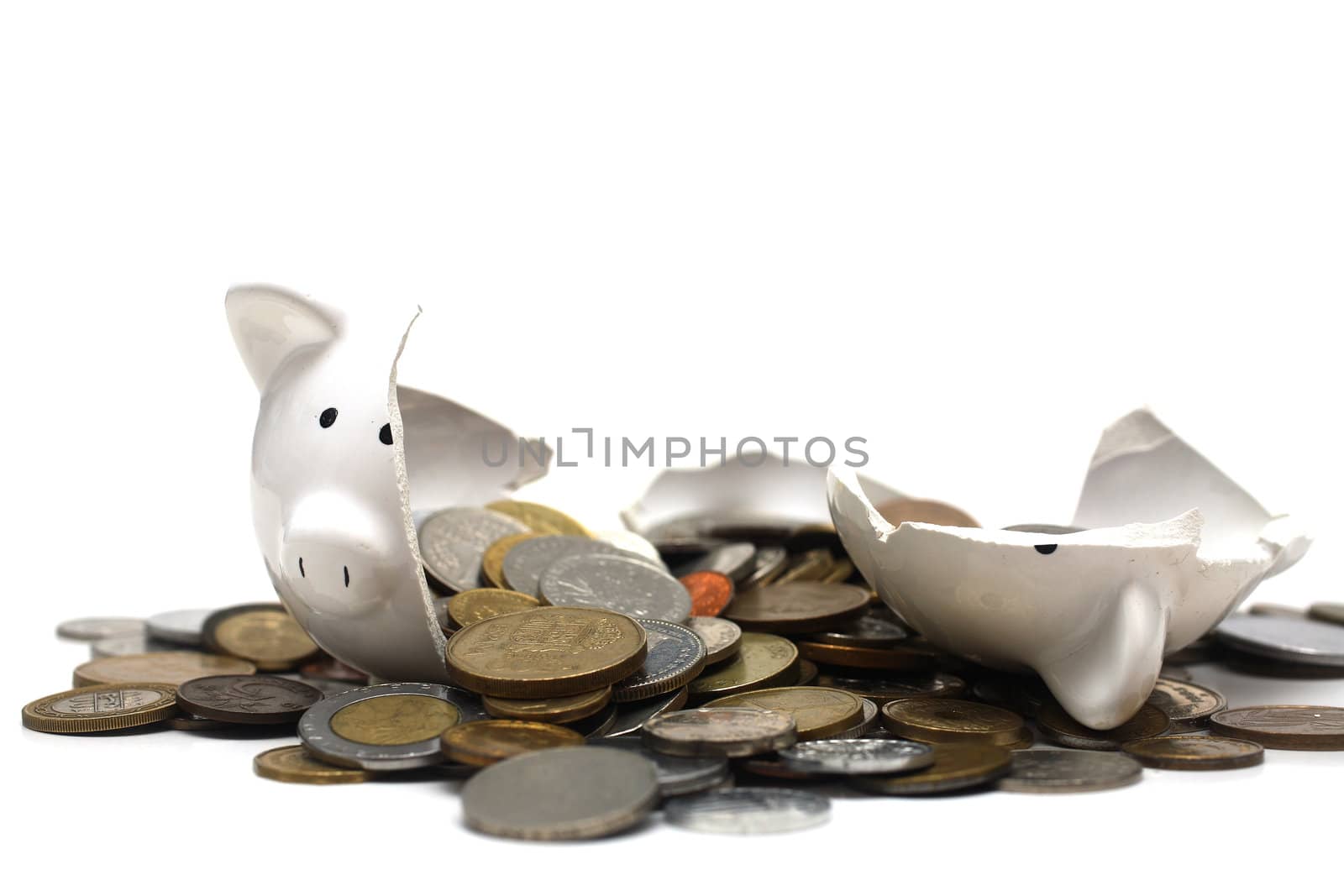 A broken piggy bank isolated on a white background with loads of coins from around the world.