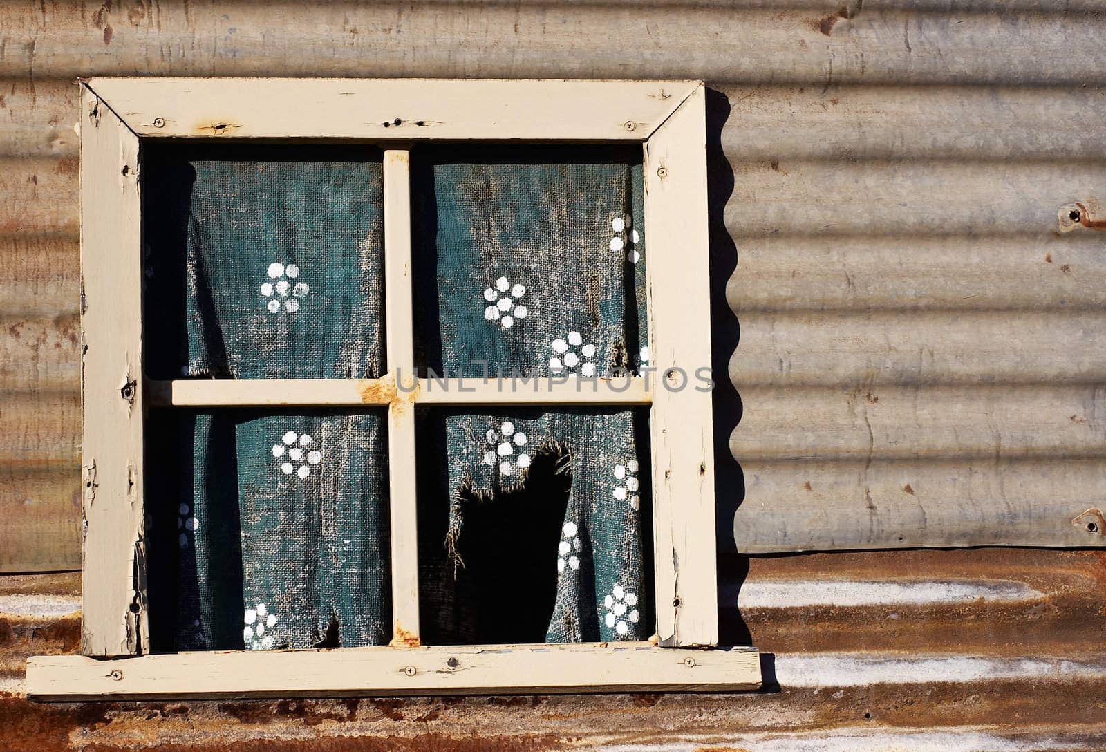an old forlorn window with ripped and worn curtain in the wall of an iron house