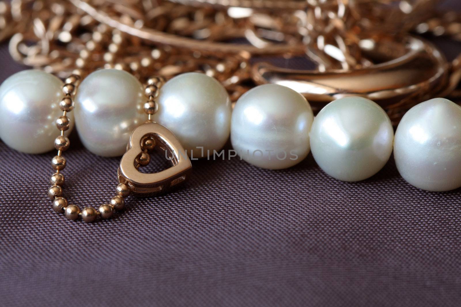 Closeup of various gold and pearl jewelry on brown textiles background