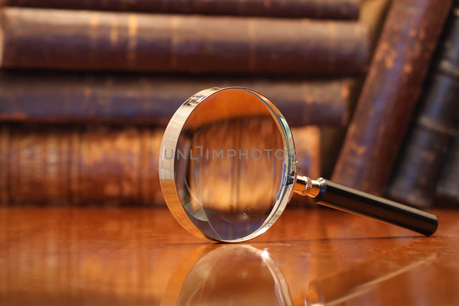 Still life with magnifying glass standing on wooden table on background with old books