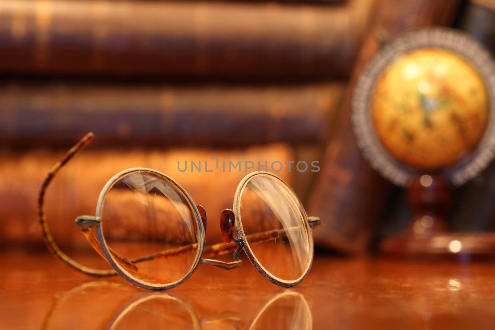 Vintage still life with old spectacles lying on wooden table on background with books and globe