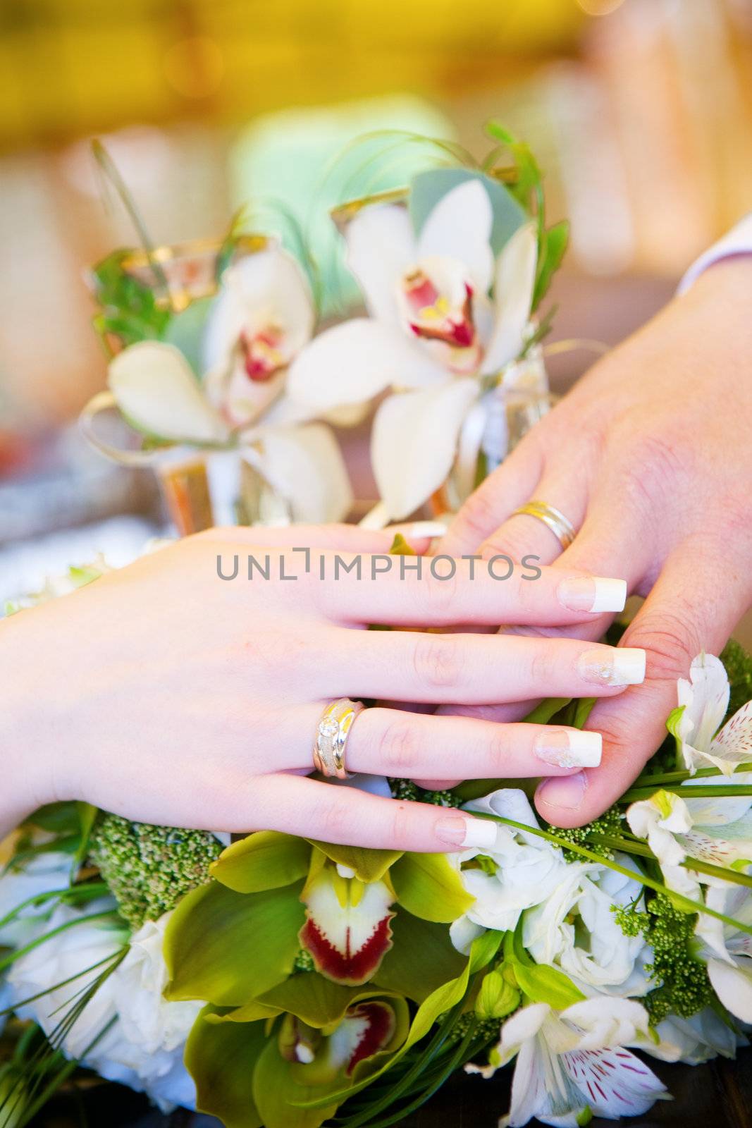 a hand of a groom and a hand of the bride with wedding rings on the flower bouquet