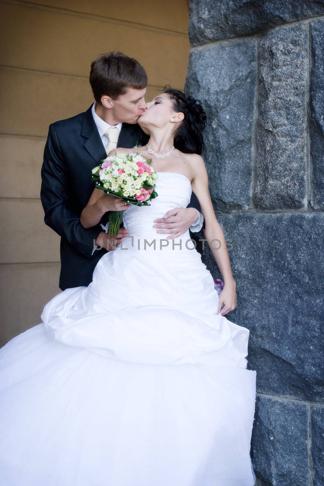 a bride and a groom stand by a wall and kiss