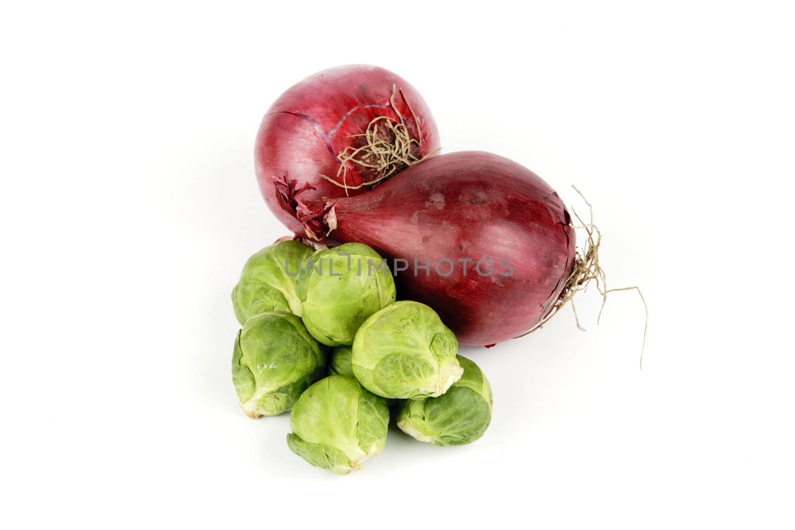 Two raw unpeeled red onions with a small pile of green sprouts on a reflective white backgrounds