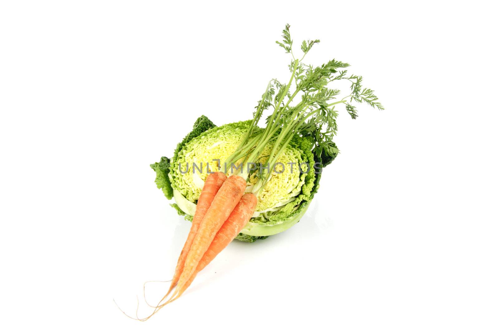 Half a raw green cabbage with a bunch of raw carrots on a reflective white background