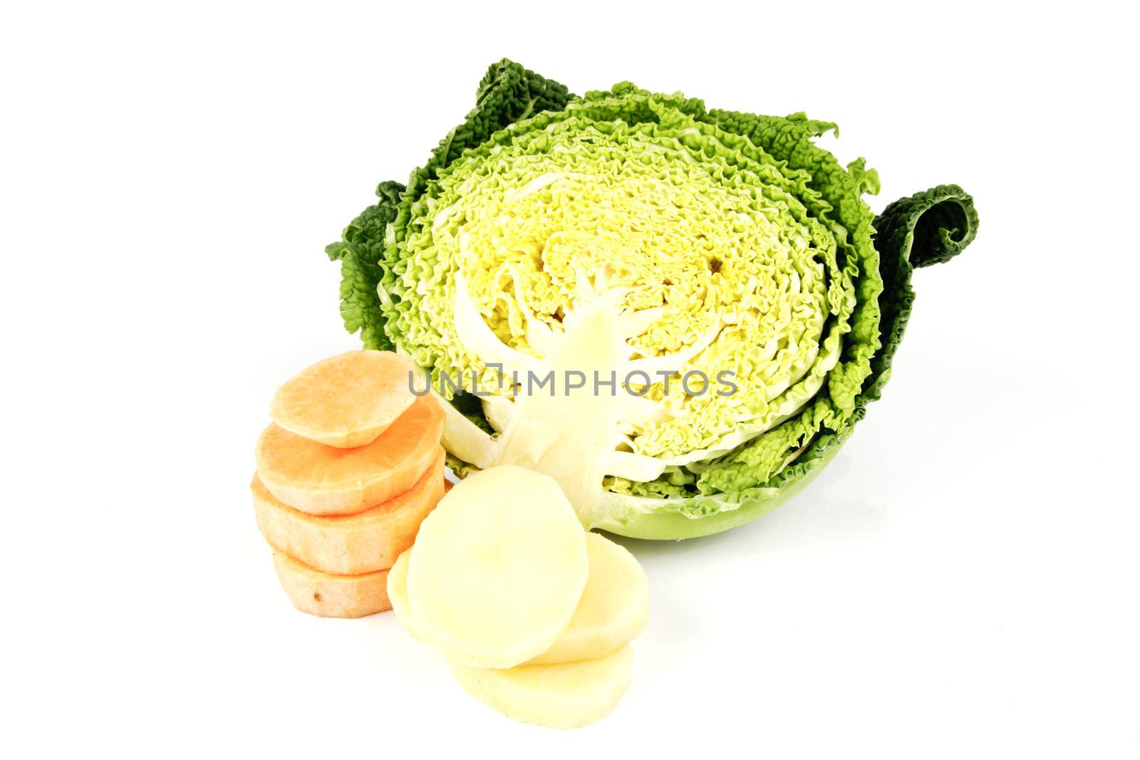 Half a raw green cabbage with potato and sweet potato slices on a reflective white background