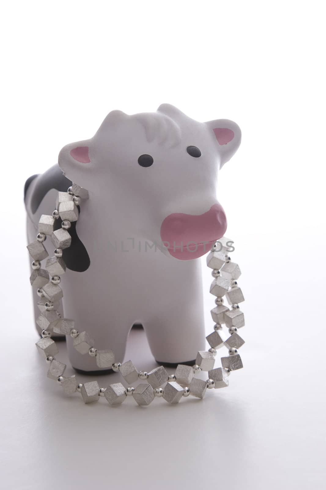 small black and white toy cow against white background wearing a silver necklace