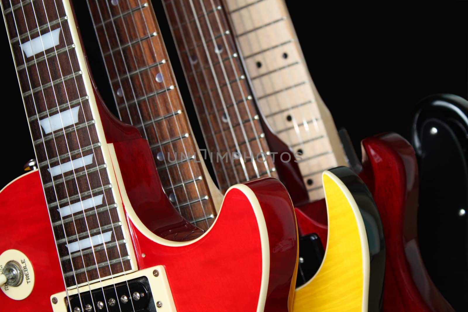 Closeup of four electric guitars isolated over a black background.