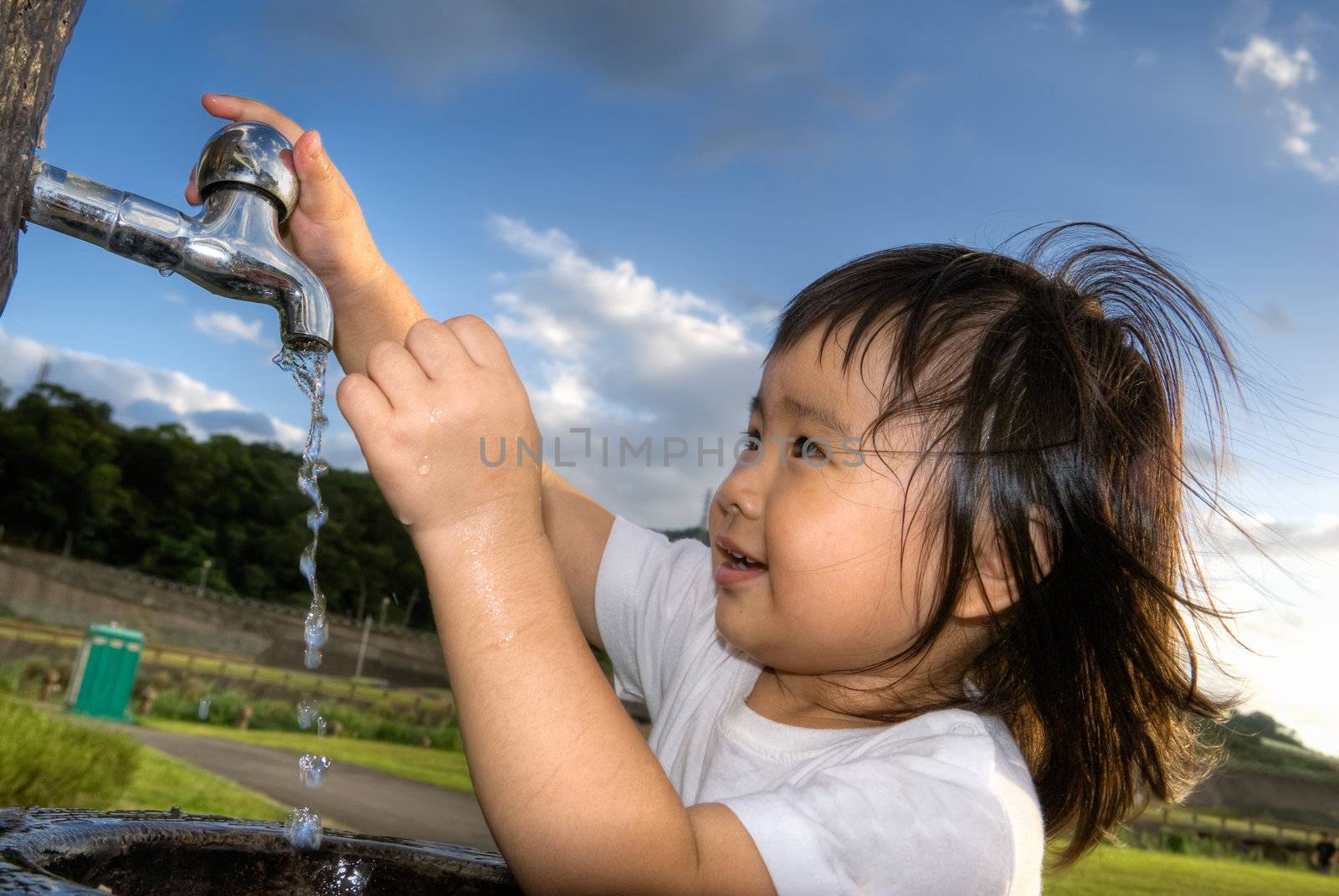 Cute Asian children wash hands in park.