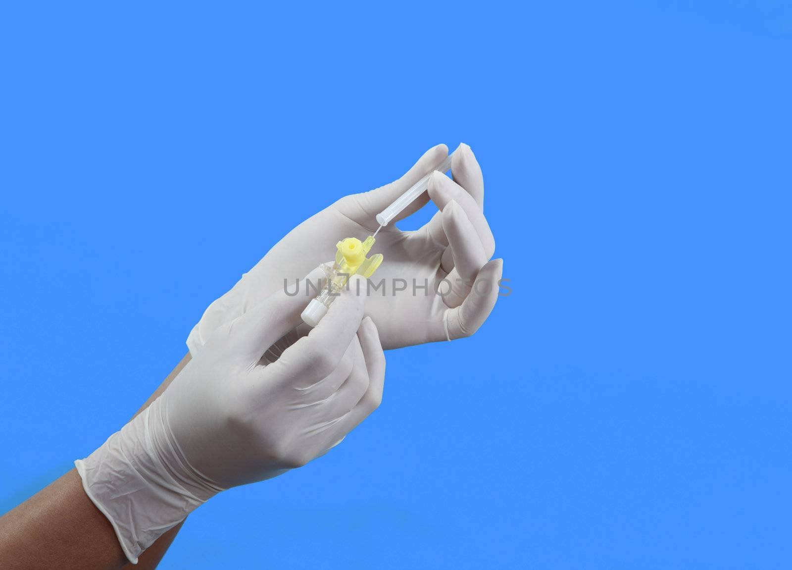 Hand in surgical gloves preparing a small intravenous puncture needle against a blue background.