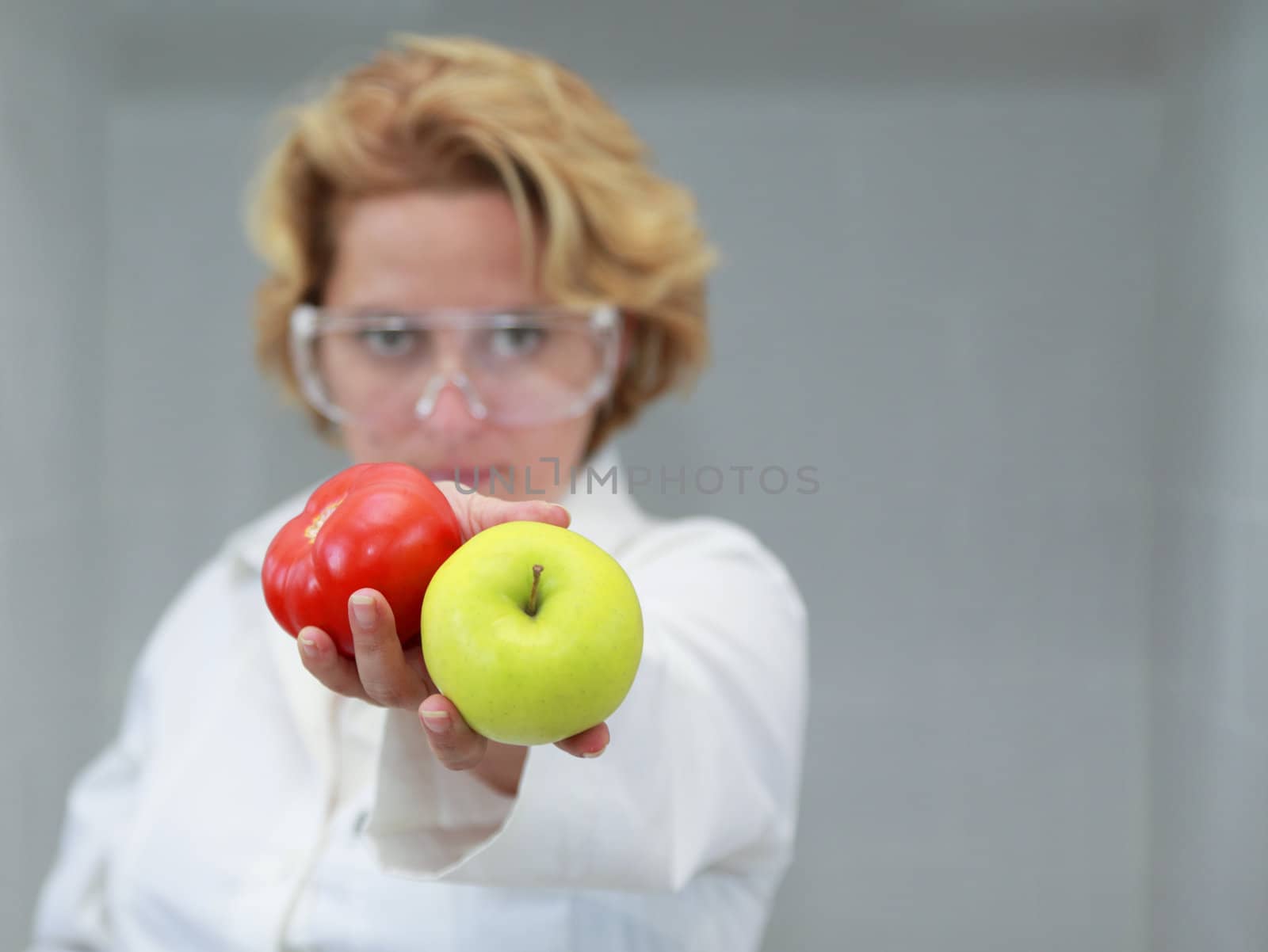 Image of a female researcher offering a tomatoe and an apple to suggest the ideea that healthy eating is recommended also by scientists.Specific lighting for a classical research laboratory.