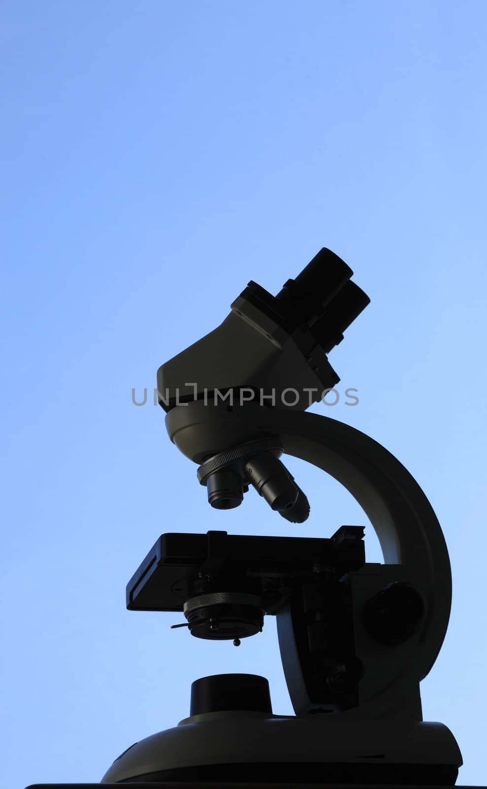 Black silhouette of a microscope against a blue sky.