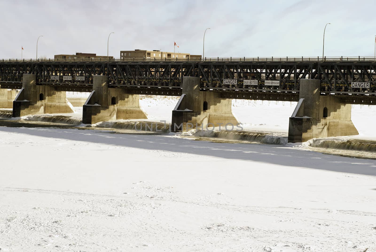 An open dam with flowing water during the winter with the rest of the river frozen.