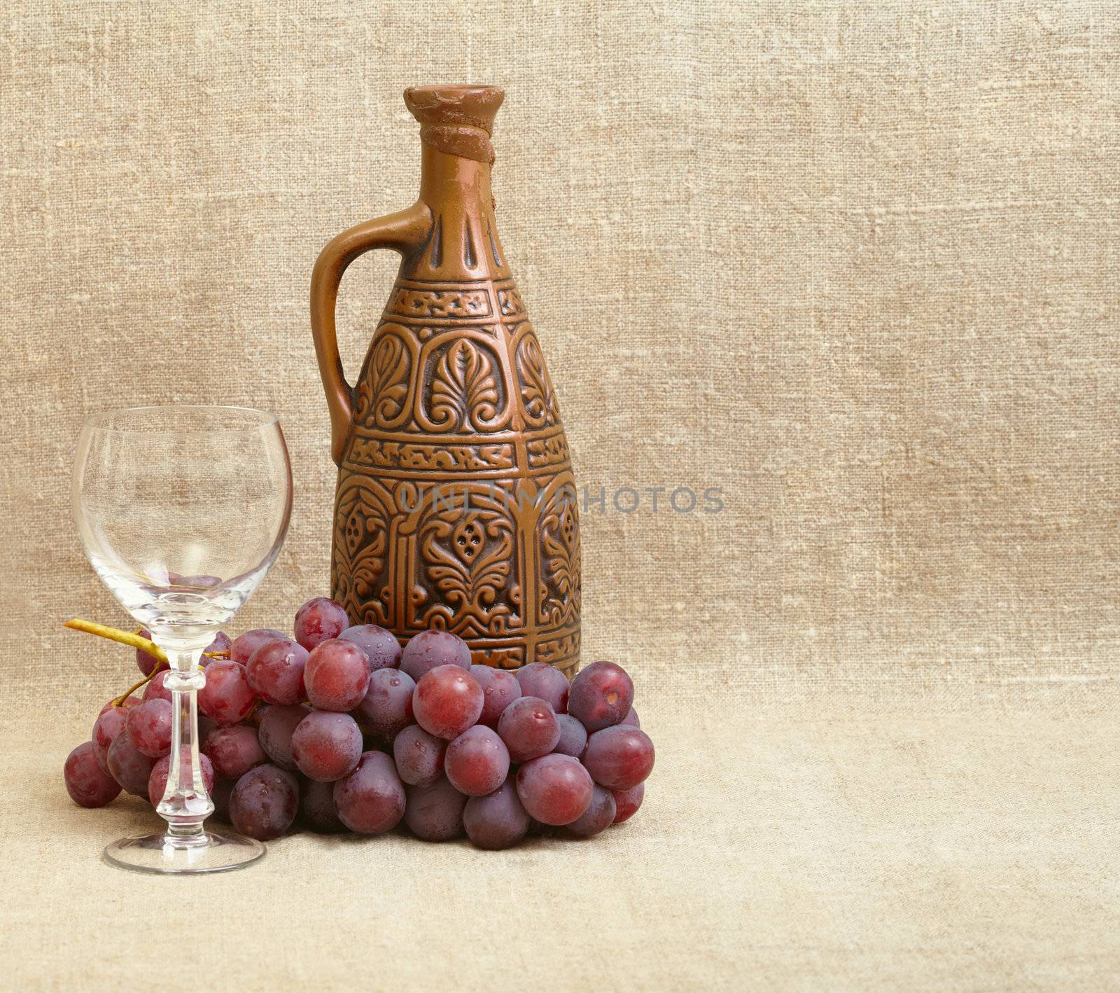 Clay bottle, grapes and a glass on the background of canvas