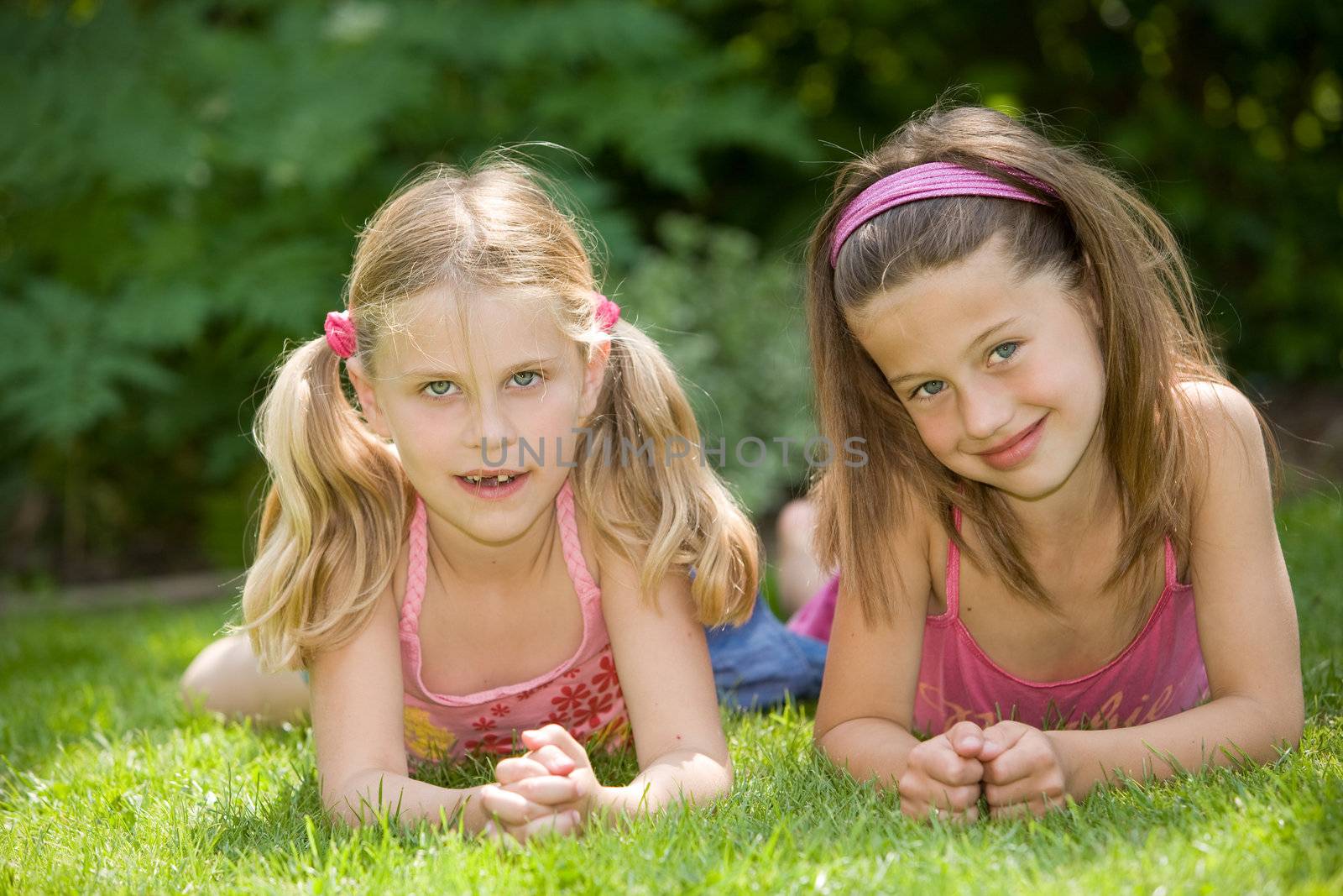 Two cute young girls lying in the grass together on a summer day