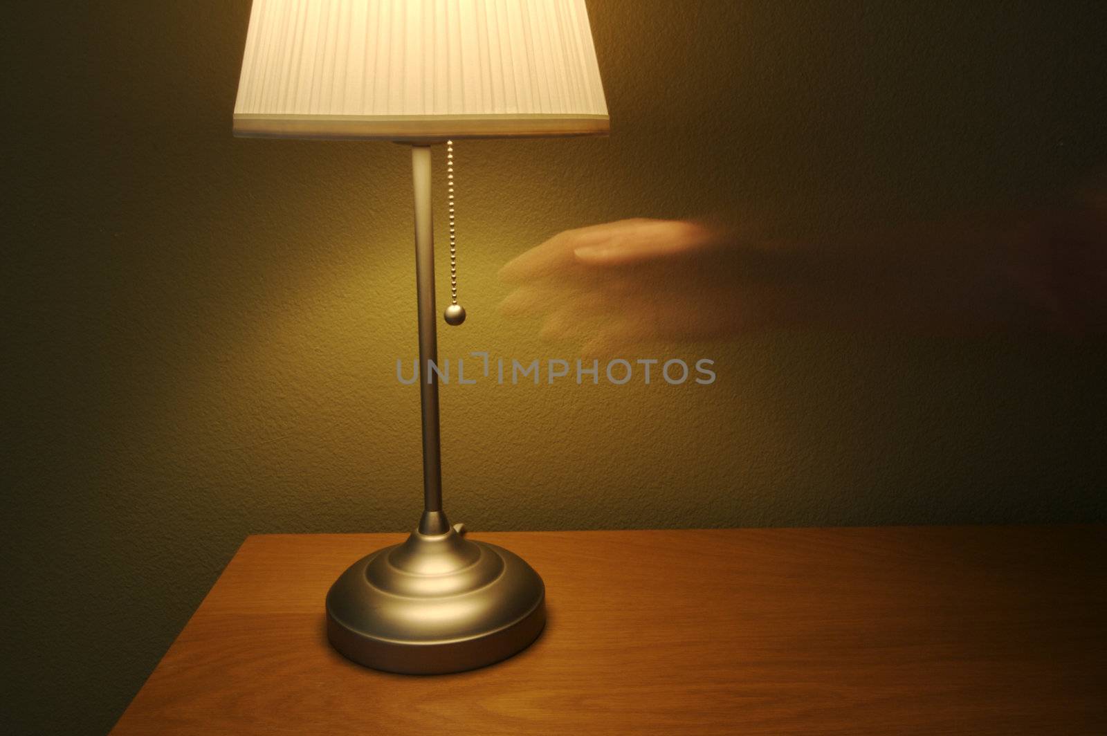 Abstract of modern lamp against green wall on wood table. Ghosted hand reaches for light switch.