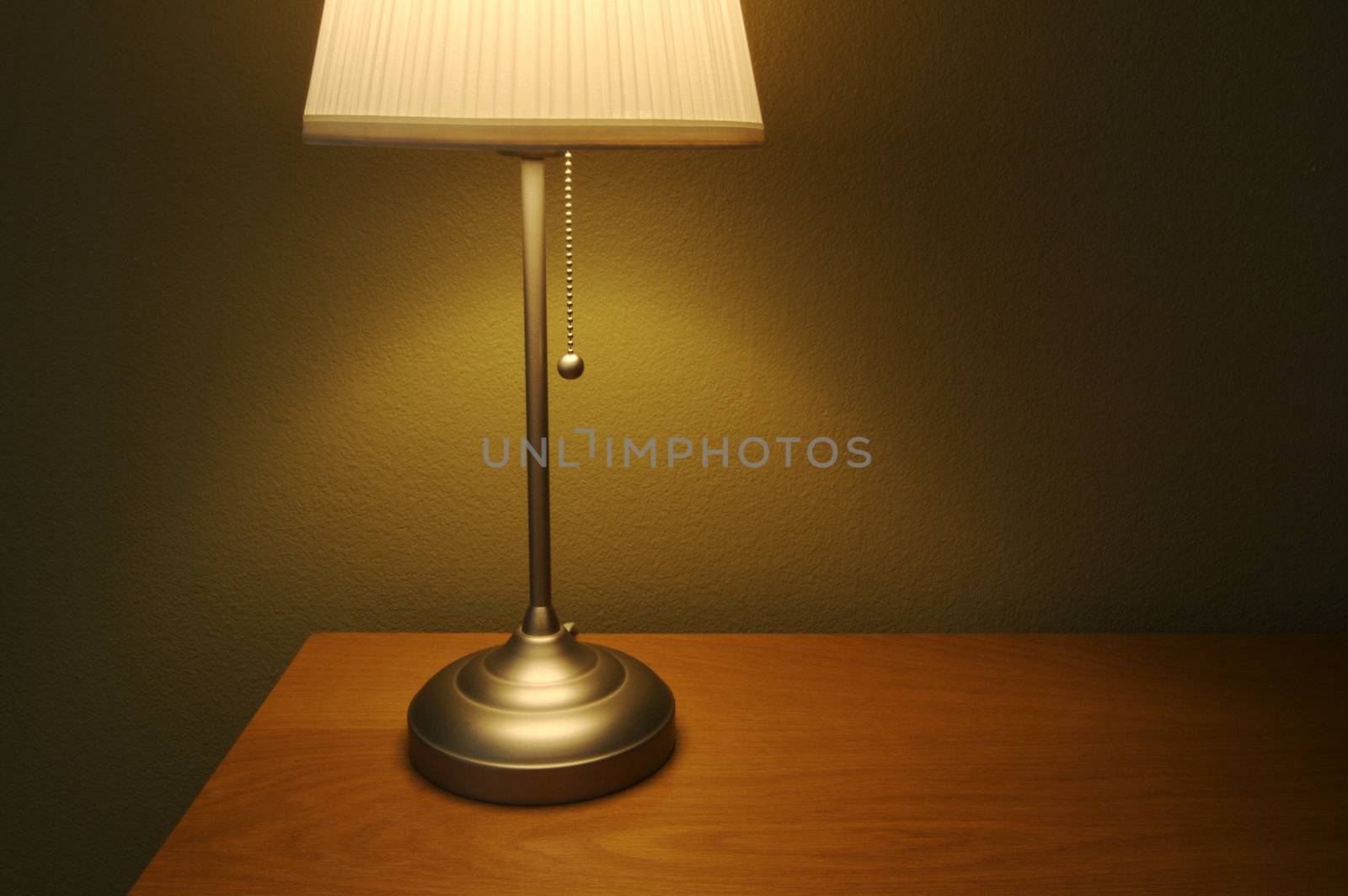 Warm lighting fills this comfortable modern lamp scene with wood desk/table and olive painted wall.