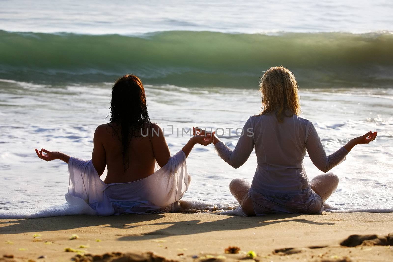 The blonde and brunette meditate on a beach