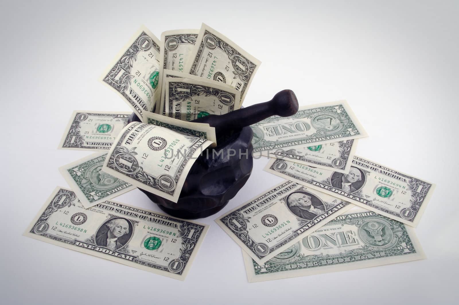 Grinding for Dollars - Wood mortar and pestle containing dollar bills on a white background.