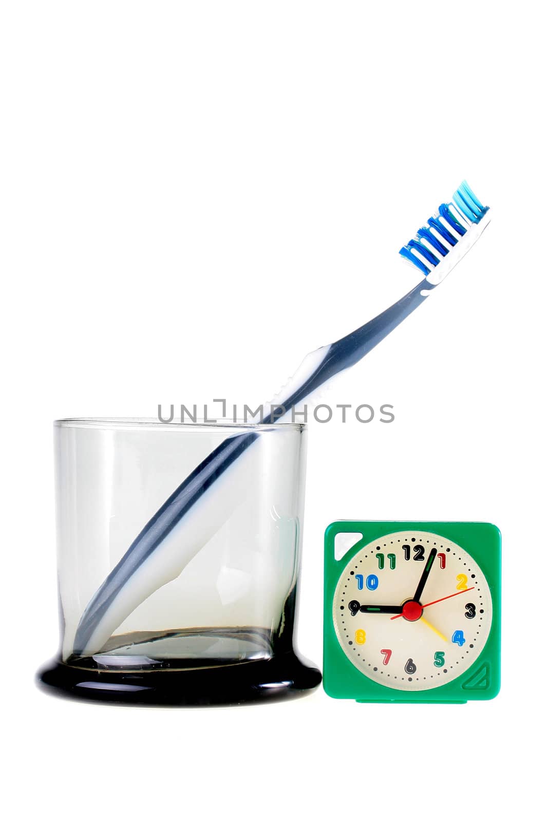Tooth-brush in a glass glass and nearby an alarm clock, a background white.