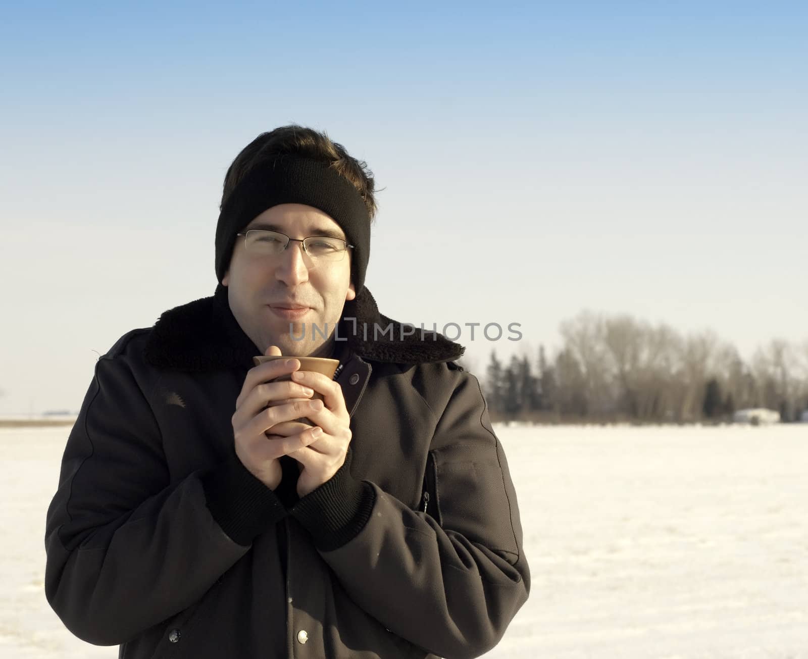 A young man warming his hands on a cup of coffee while standing outside in the winter.