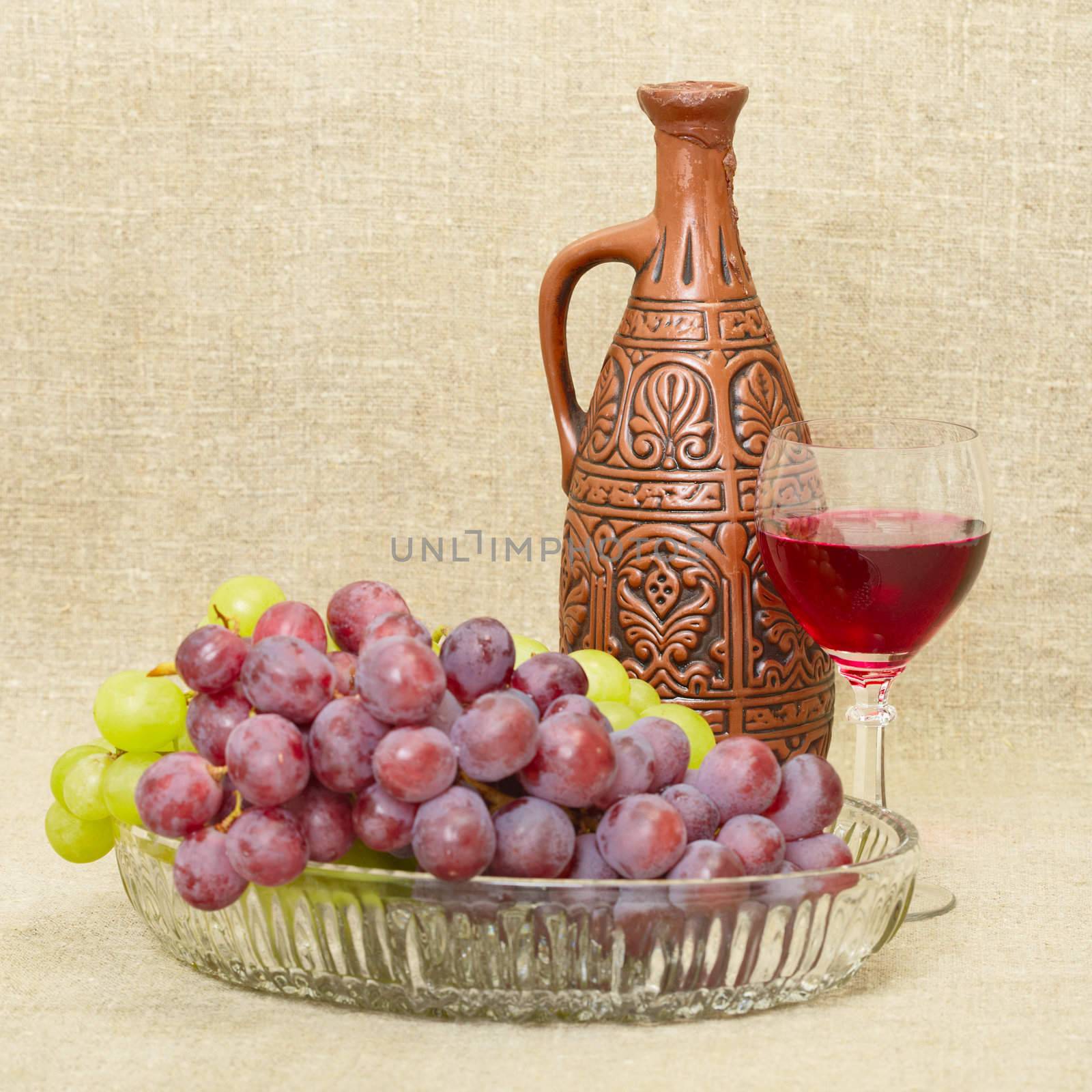 Still life with ceramic bottle, grape and glass on canvas background