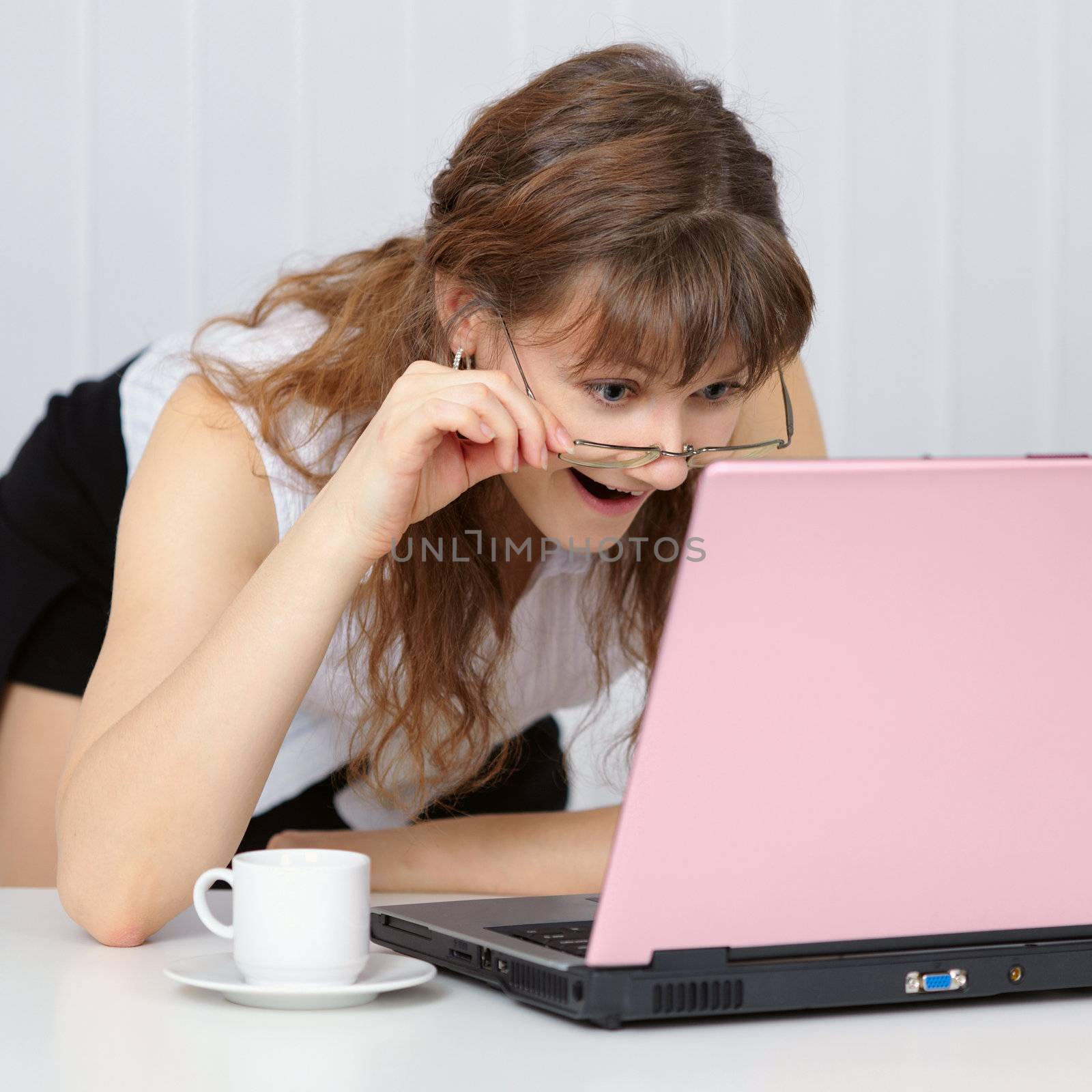 Young woman working with pink laptop computer sitting at the table