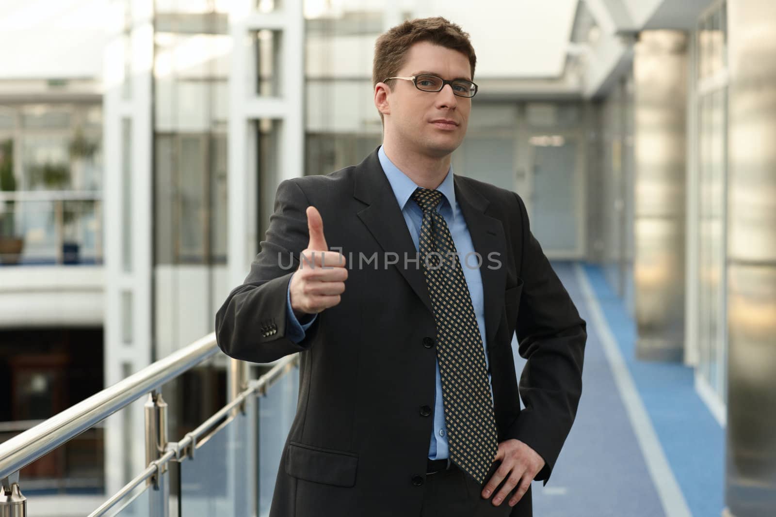 Portrait of young businessman in modern business office building corridor showing OK success