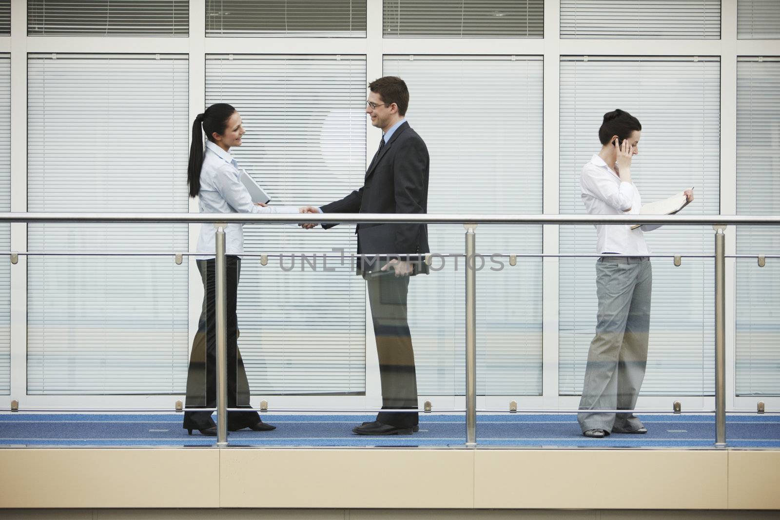 Businessman and businesswoman shaking hands on modern office corridor. tree persons