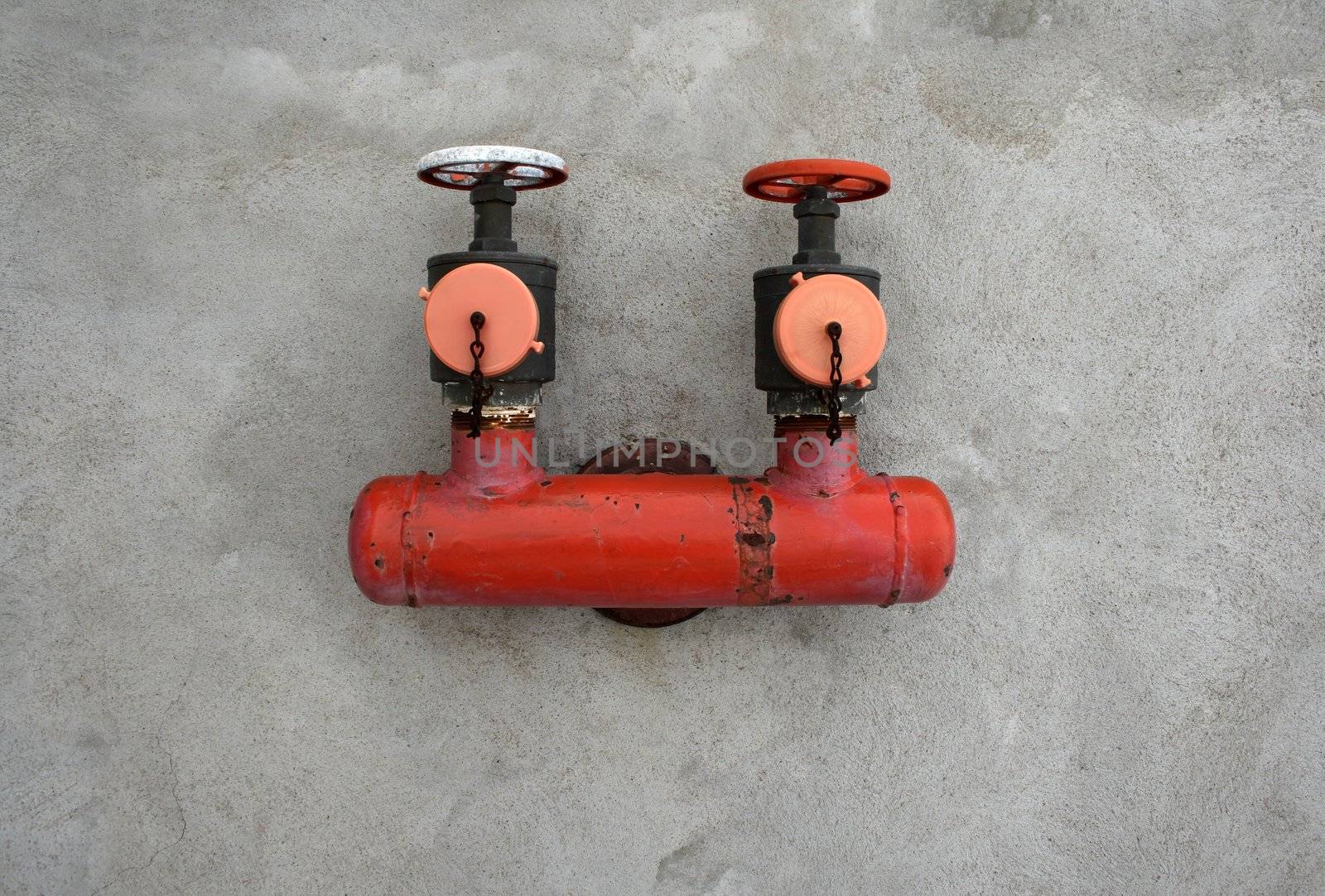 Red iron valve on a gray concrete wall.