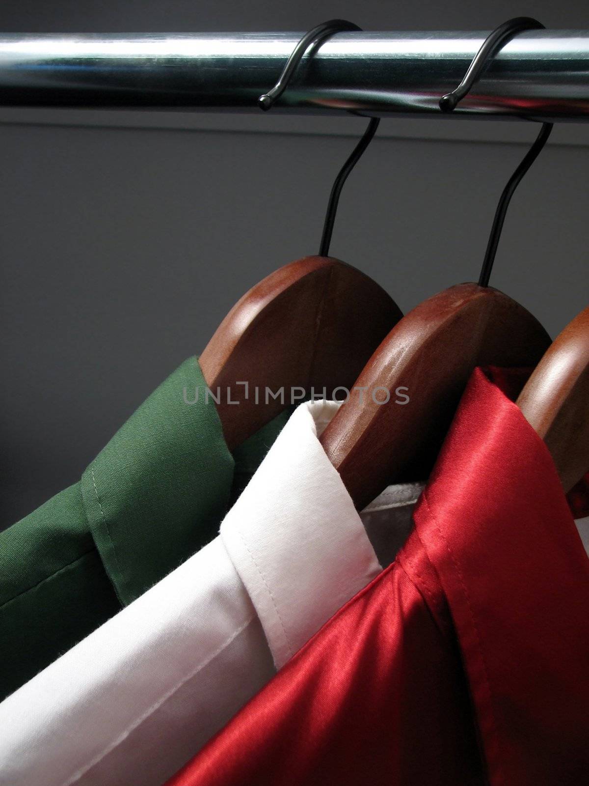Colors of Italian flag: green, white and red shirts on wooden hangers in a closet.