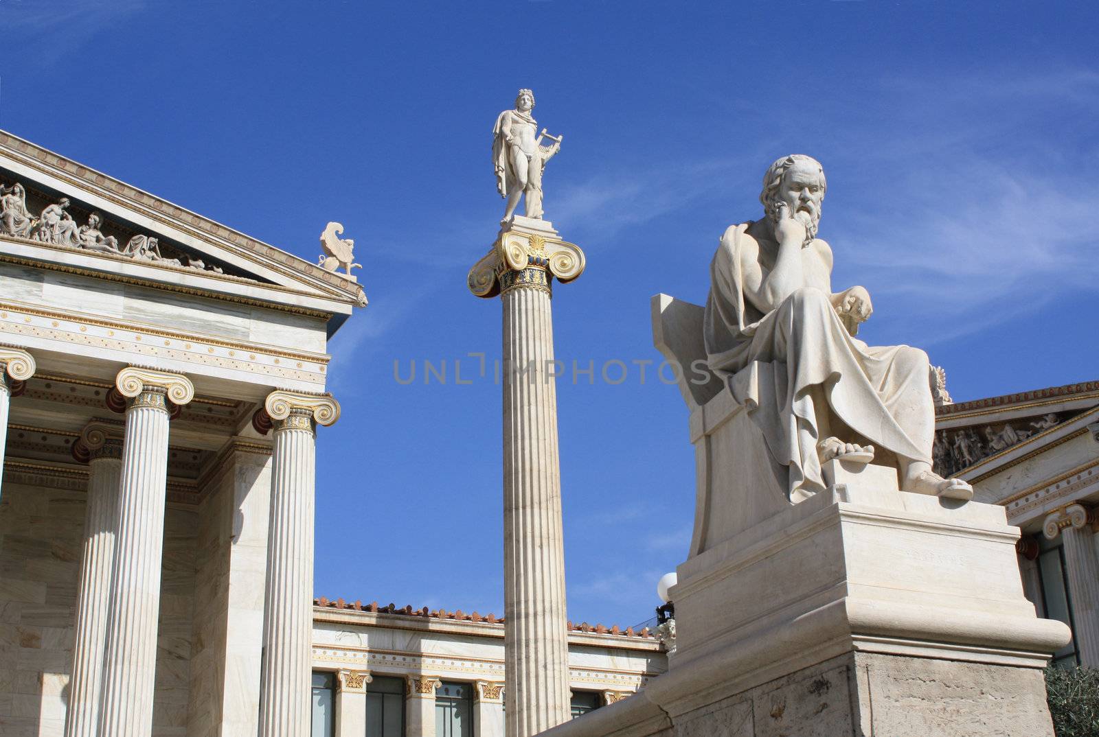 Image shows part of the main building of the Academy of Athens with ionic columns, statue of god Apollo on top of a pillar with his guitar and ancient Greek philosopher Socrates sitting. This neoclassical construction is one of the major landmarks of Athens.