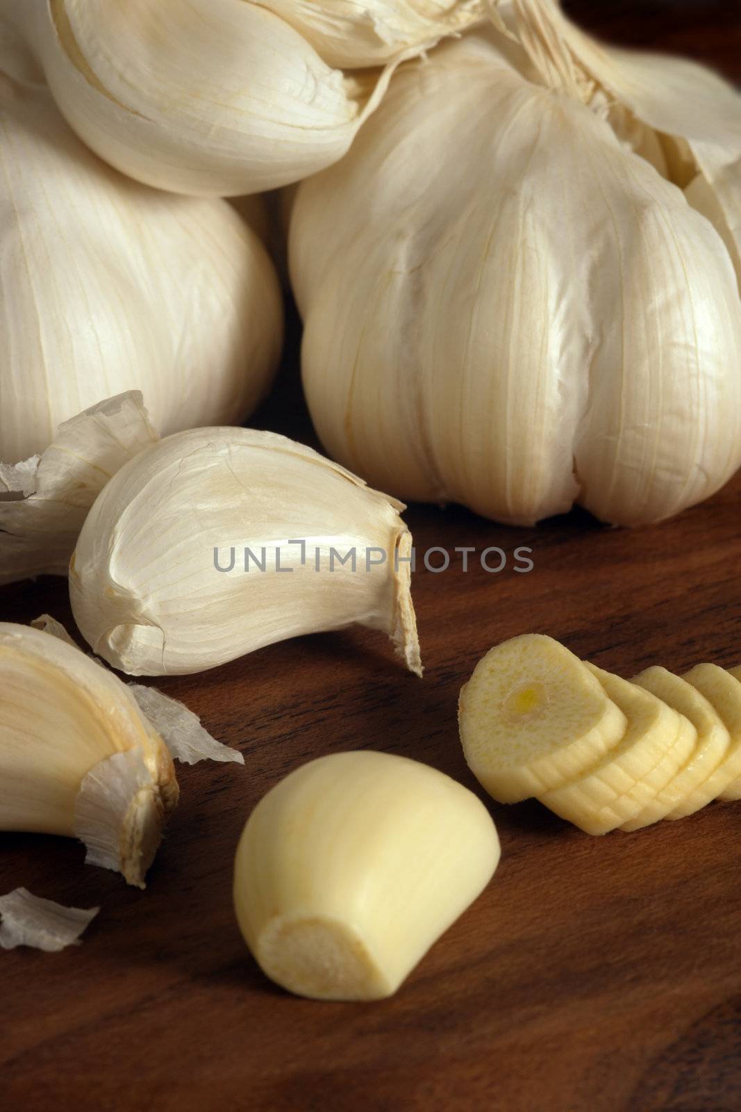 Cloves and sliced garlic on a wood cutting board.
