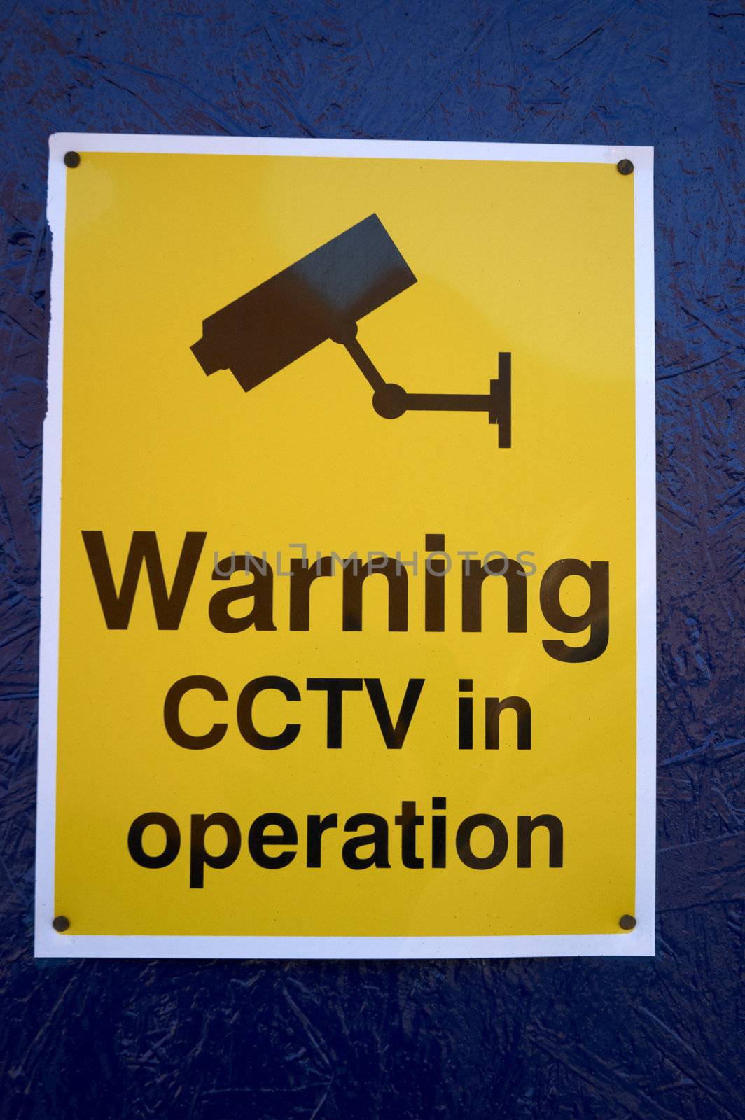 A cctv warning sign on a blue wall