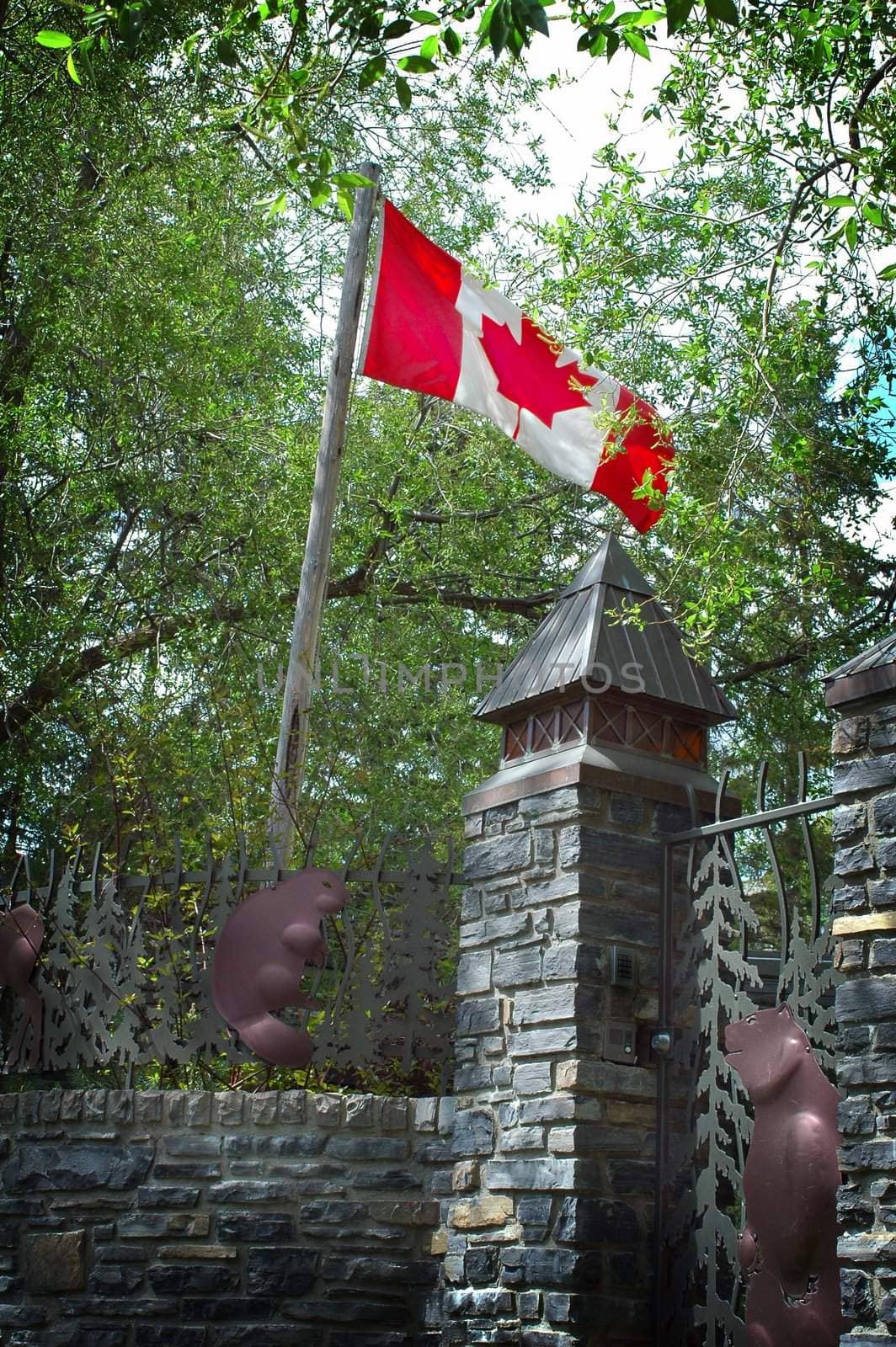 Image of Canadian flag and stone fence with Beaver and Bear art on associated fence.