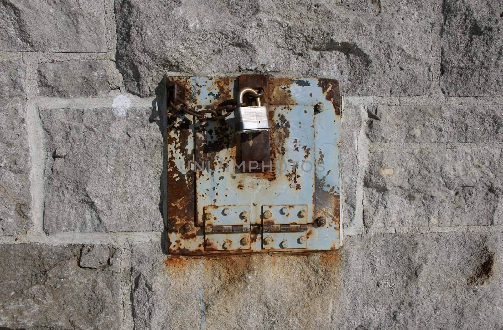 Iron lock and rusty chain on a stone wall by anikasalsera