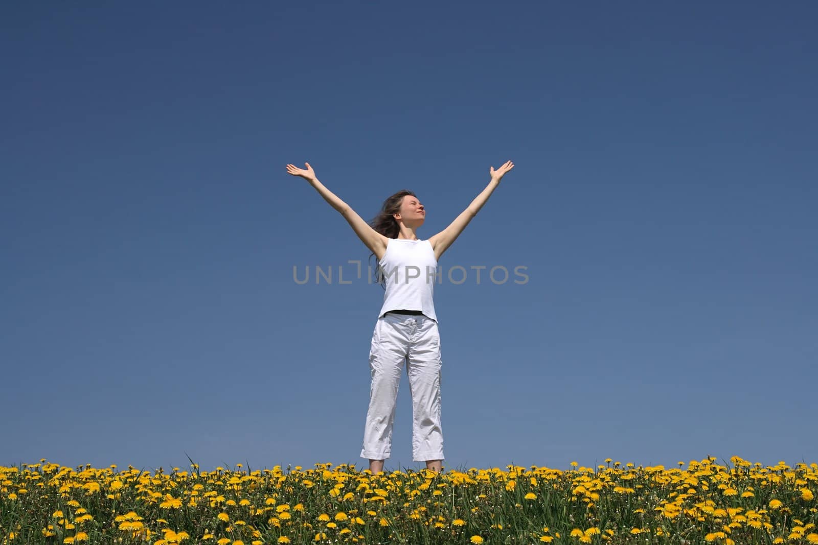 Young woman greets the sun in the morning, in a flowering spring field.