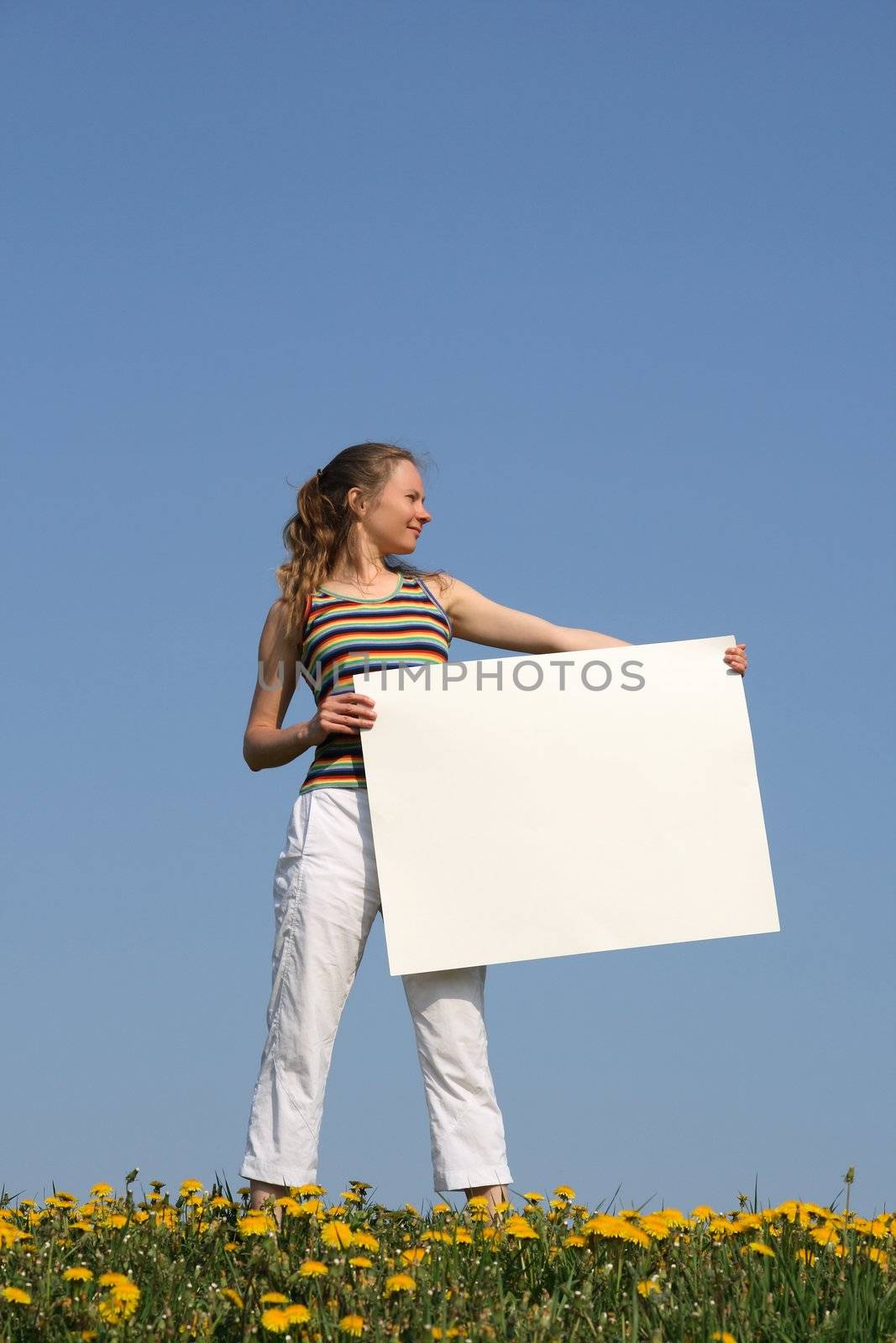 Young woman in dandelion field holding blank cardboard with copyspace.